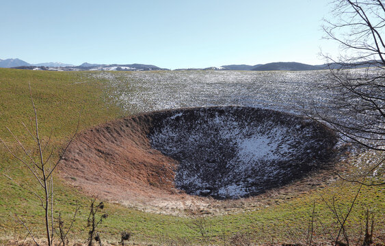 large depression in the terrain with snow in the mountains caused by the explosion of a mine