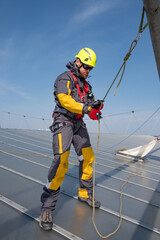 Male worker on roof prepares ropes for belaying, checks fasteners. Middle aged caucasian guy...
