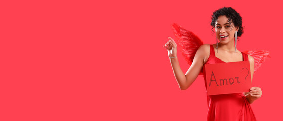 Young woman dressed as cupid holding paper with word AMOR on red background with space for text....