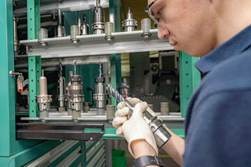 To operate a CNC machine, a worker selects and inspects the required cutter from the rack and tool...
