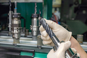 A worker inspects and selects a cutter from a rack to use on a CNC machine.
