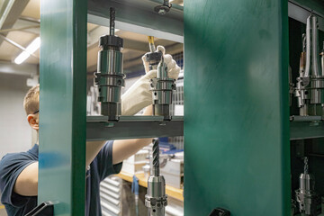 To operate a CNC machine, a worker selects and inspects the required cutter from the rack and tool...