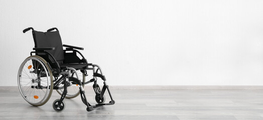 Modern empty wheelchair near white wall. Banner for design