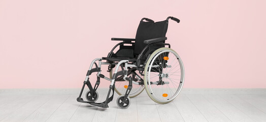 Modern empty wheelchair near pink wall
