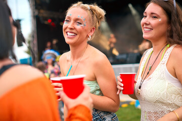 Three Female Friends Wearing Glitter Having Fun At Summer Music Festival Holding Drinks