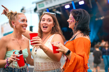 Three Female Friends Wearing Glitter Having Fun At Summer Music Festival Holding Drinks