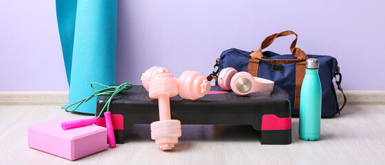 Sports equipment with headphones and bag near lilac wall in gym