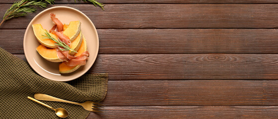 Plate with tasty melon, prosciutto and rosemary on brown wooden background with space for text