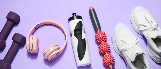 Water bottle with sports equipment, headphones and sneakers on violet background