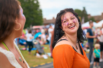 Two Female Friends Wearing Glitter Having Fun At Summer Music Festival Doing Cheers With Drinks