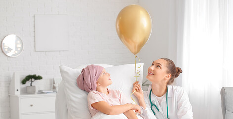 Doctor with golden balloon and little girl undergoing course of chemotherapy in clinic