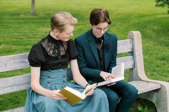 A lovely LGBT couple reading a booking on a bench in the park.