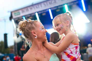 Mother With Daughter Wearing Glitter Having Fun At Outdoor Summer Music Festival
