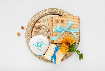 Passover Seder plate with flatbread matza, kippah, walnuts and flowers on white background