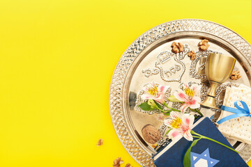 Passover Seder plate with Torah, wine cup, flatbread matza and flowers on yellow background