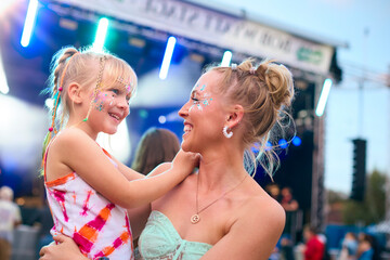 Mother With Daughter Wearing Glitter Having Fun At Outdoor Summer Music Festival