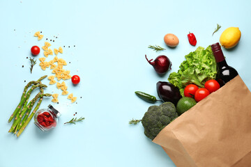Paper bag with vegetables, fruits and wine bottle on light blue background