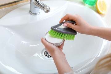 Woman cleaning white ceramic sink with brush and baking soda, closeup