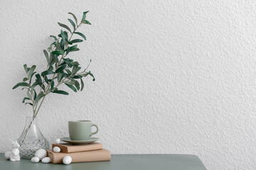 Vase with plant branches, Easter eggs, bunny and cup near white wall