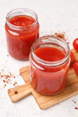 Jars with tasty tomato sauce on light background