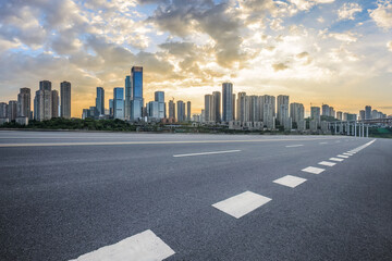 Empty asphalt road and city buildings skyline at sunset