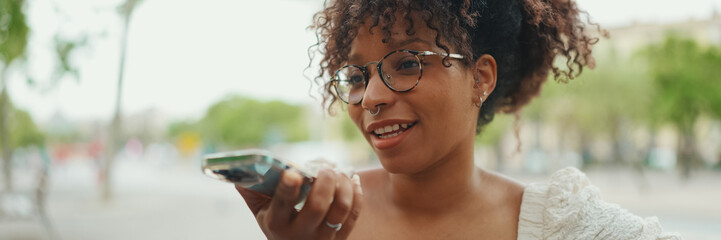 Closeup portrait of a young woman in glasses sits on a bench smiling and sends a voice message....