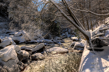 Flowing stream in winter through snow covered woods