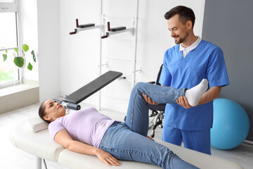 Male physiotherapist working with young woman on couch in rehabilitation center
