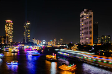 Fototapeta na wymiar Night light landscape along the Chao Praya River, having some boats come to celebrate the New Year eve on the Asiatique landmark side in Bangkok city, Thailand.