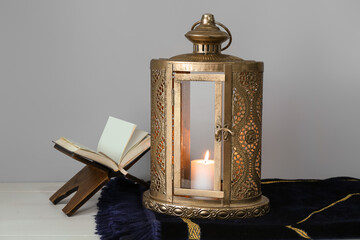 Fanous with burning candle, Koran and prayer mat on light wooden table. Islamic New Year celebration