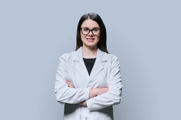 Woman medical scientist, pharmacist in white coat with crossed arms on grey background