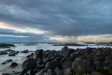 Fototapeta na wymiar Long exposure view of waves crashing on the rocky shore of Benares beach during a rainy morning in Mauritius island