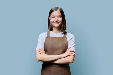 Young smiling woman in apron looking at camera on blue studio background