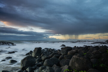 Long exposure shot of the waves crashing on the rocky shore and the rain clouds approaching the...