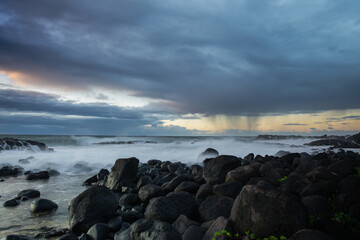 Long exposure shot of the waves crashing on the rocky shore and the rain clouds approaching the...