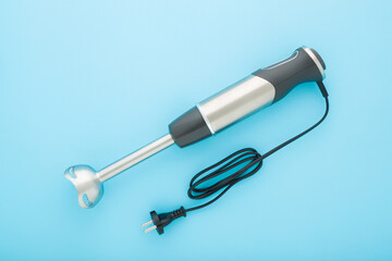 New hand blender with black wire on light blue table background. Pastel color. Closeup. Kitchen electrical appliance for fruit, vegetable, meat or other food blending. Top down view.