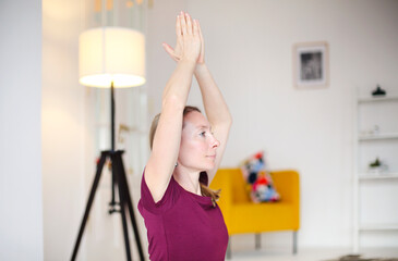 Young calm caucasian blonde lady practicing yoga in living room at home