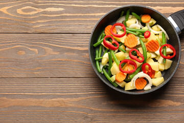 Frying pan with fresh vegetables on wooden background