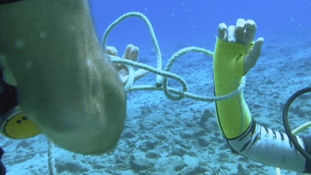 scuba diving instructor demonstrates student how to tie node underwater during teaching course in blue ocean water in the ocean blue sea salt water world during day time with sunlight hue sun reflect