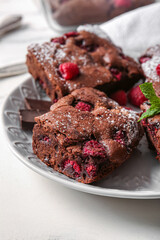 Plate with pieces of raspberry chocolate brownie on white background