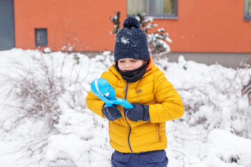 Fototapeta na wymiar Winter games outdoors. Small boy have fun making snowballs with toy plastic maker.