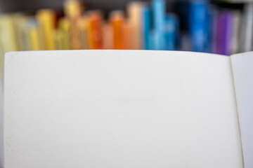 Blank page of a book with out of focus colorful bookshelves on the back. Copy space