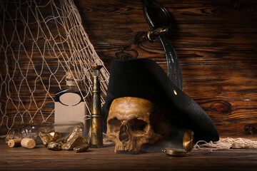 Human skull with pirate hat, golden nuggets, bottle of rum and travel equipment on brown wooden...