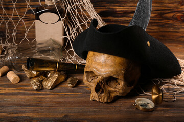 Human skull with pirate hat, golden nuggets, bottle of rum and travel equipment on brown wooden background