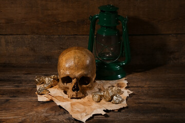 Human skull with oil lamp, old manuscripts and golden nuggets on brown wooden background