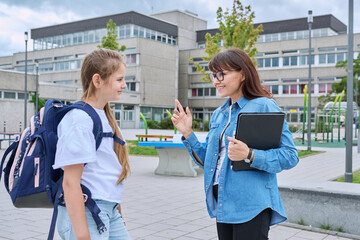 Talking teacher and schoolgirl child outdoor, school building background