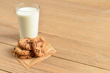 Tasty cookies with chocolate chips and glass of milk on wooden background