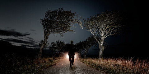 Männliche Person auf einer Waldstrasse im Scheinwerferlicht als Schemenhafte Silhoutte - obrazy, fototapety, plakaty
