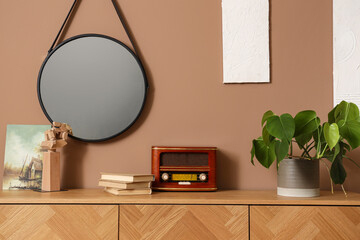 Wooden cabinet with radio, decorative wooden hand and mirror near brown wall