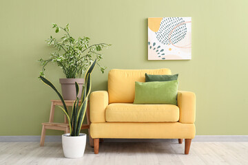Yellow armchair with cushions and houseplants near green wall